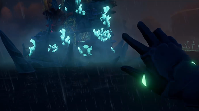 A player's gloved hand held up in first-person, a craggy spire in the background with blue coral on it.