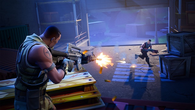 A player hiding behind pallets shoots at another player running across a warehouse floor