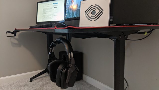 An angled shot of the ergonomic desk, showing the headset hook and headset, cupholder, monitors.