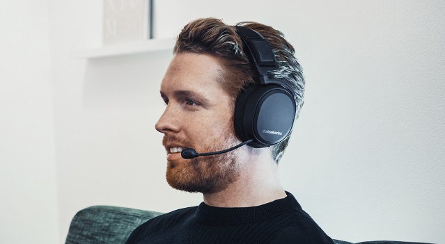 Man in black shirt wears Arctis Pro Wireless while sitting on couch
