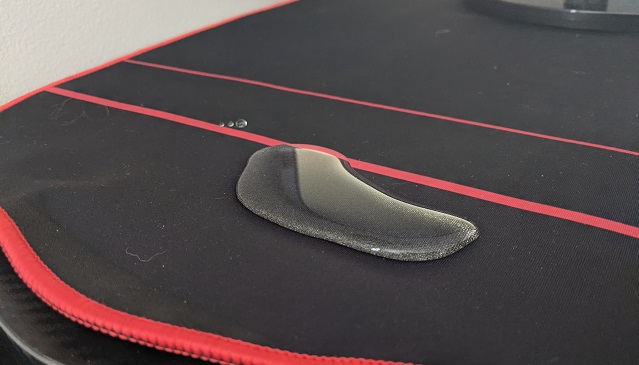 A small water puddle on the desk's red and black mousepad.